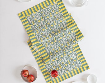 Puede incluir: Vista aérea de una mesa con dos manteles individuales estampados en verde y amarillo. Los manteles individuales tienen un diseño de hojas y limones. Platos, cuencos y cubiertos blancos están dispuestos alrededor de los manteles individuales. Dos granadas están en un cuenco blanco.
