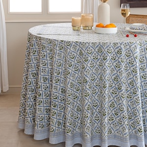 May include: A round tablecloth with a blue and white floral pattern. The tablecloth is on a round table with a white vase, candles, and a bowl of oranges. The tablecloth has a blue and white striped border.