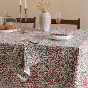 Puede incluir: Un mantel rectangular con un patrón floral repetitivo en rojo oscuro y verde oliva sobre un fondo blanco. El diseño incluye motivos botánicos intrincados y un borde decorativo, extendido sobre una mesa con servilletas plegadas a juego.