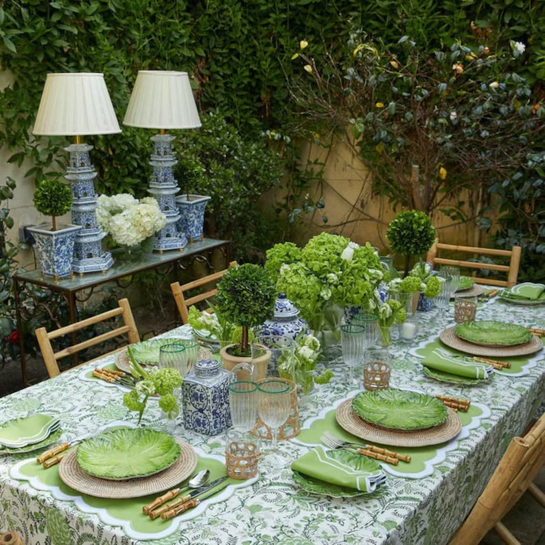 May include: A green and white patterned tablecloth with green and white plates, green napkins, and bamboo cutlery. A table setting with green plants and white flowers in a vase.