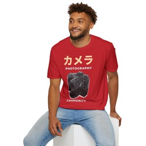 Könnte beinhalten: Ein rotes T-Shirt mit einer Grafik einer Kamera und dem Text "カメラ PHOTOGRAPHY COMMUNITY".