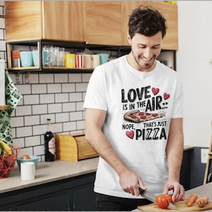 Könnte beinhalten: Weißes T-Shirt mit einem Grafikdruck einer Pizzastückes und dem Text "Love is in the air... Nope, that's just pizza".