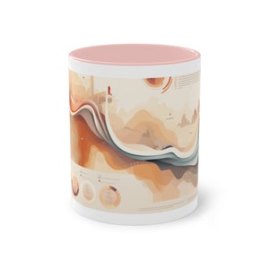 May include: A white ceramic mug with a pink rim and a colorful abstract design. The design features a landscape with mountains, waves, and geometric shapes in shades of orange, brown, blue, and white.