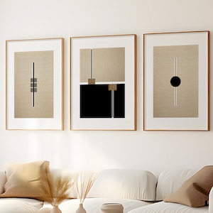 May include: Three framed abstract art prints with geometric shapes and lines in black, white, and brown on a beige background. The prints are hung on a white wall above a white couch.