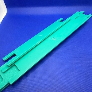 May include: Two green plastic track pieces for a toy train set. The pieces are connected together and have a textured surface.