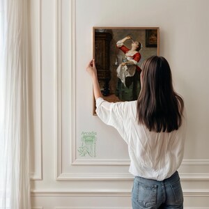 Puede incluir: Una impresi&oacute;n art&iacute;stica rectangular enmarcada que representa a una persona con corpi&ntilde;o rojo y falda verde sosteniendo una bandeja y bebiendo de un vaso. La obra se exhibe en un marco de madera fino sobre una pared blanca con molduras, incluyendo el logo de Arcadia Museum.