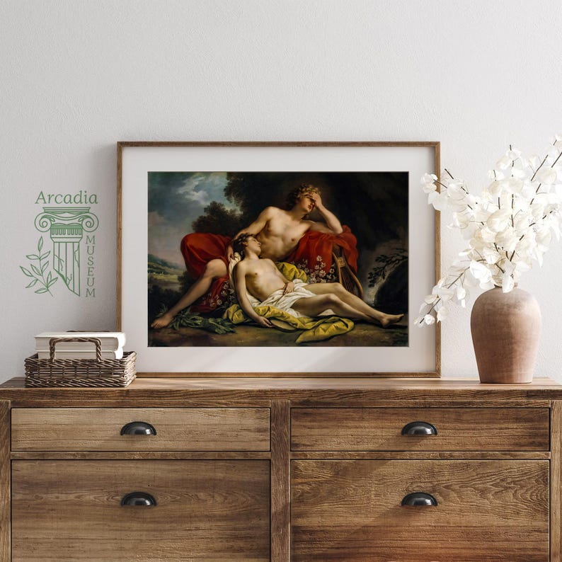 May include: A framed art print featuring a classical painting of two figures resting in a landscape, displayed on a wooden dresser next to a wicker basket of books and a vase of white flowers. The text Arcadia Museum is printed on the wall.