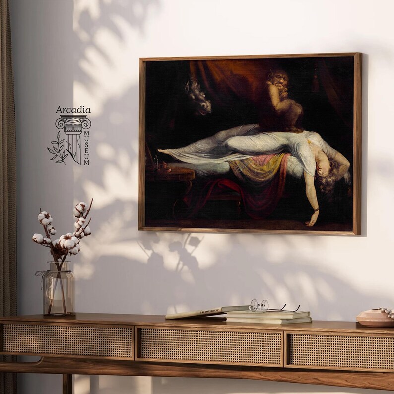 May include: A framed print of Henry Fuseli's The Nightmare painting, featuring a reclining figure in a white gown with a dark creature perched on their chest. The artwork is displayed on a wall above a wooden console table with a glass vase of cotton.