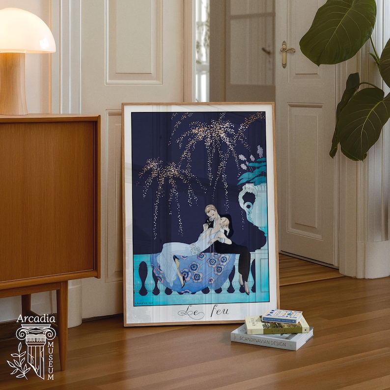 May include: A framed art print titled Le feu featuring a dark blue night sky with gold fireworks above a couple embracing on a balcony. The scene includes a blue floral patterned skirt, a white top, and a dark suit, set against a light blue railing.