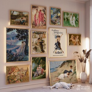 May include: A gallery wall featuring eleven framed art prints with various classical paintings, including scenes of figures in landscapes, a poster with German text, and a beach scene, displayed on a wall above a white cat lying on the floor.