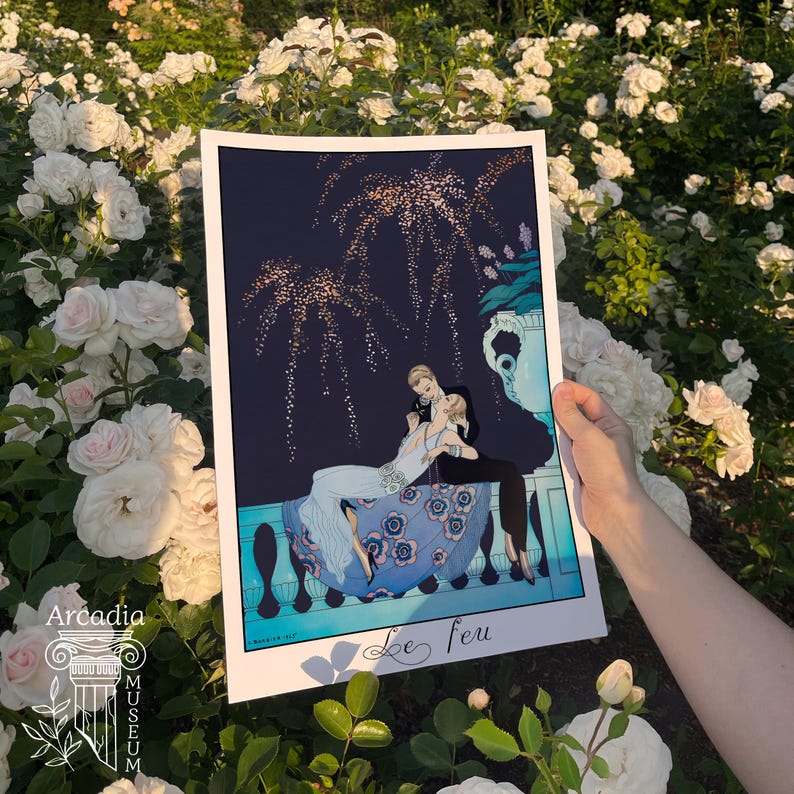May include: A rectangular art print titled Le feu featuring a dark blue night sky with gold fireworks above a couple sitting on a balcony. The illustration shows a person in a white dress and a person in a black suit with a blue floral skirt.