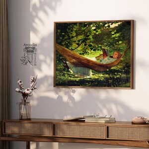 May include: A rectangular wall art print featuring an oil painting of a person in a light blue dress resting in a brown hammock while reading a book, surrounded by green foliage. The text Arcadia Museum is printed in black on the left side.