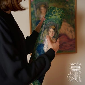 May include: A cylindrical art print featuring a reproduction of a painting depicting a person with dark hair in a garden setting with green foliage and blue accents. The print is held vertically and displays a soft, impressionistic style.