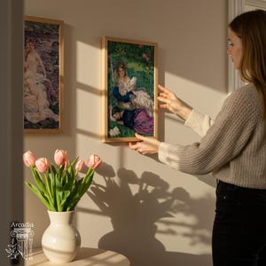 May include: Two rectangular framed art prints featuring classical paintings of figures in outdoor settings, displayed on a wall. A white ceramic vase filled with pink tulips sits on a surface in the foreground, with the Arcadia Museum logo visible.