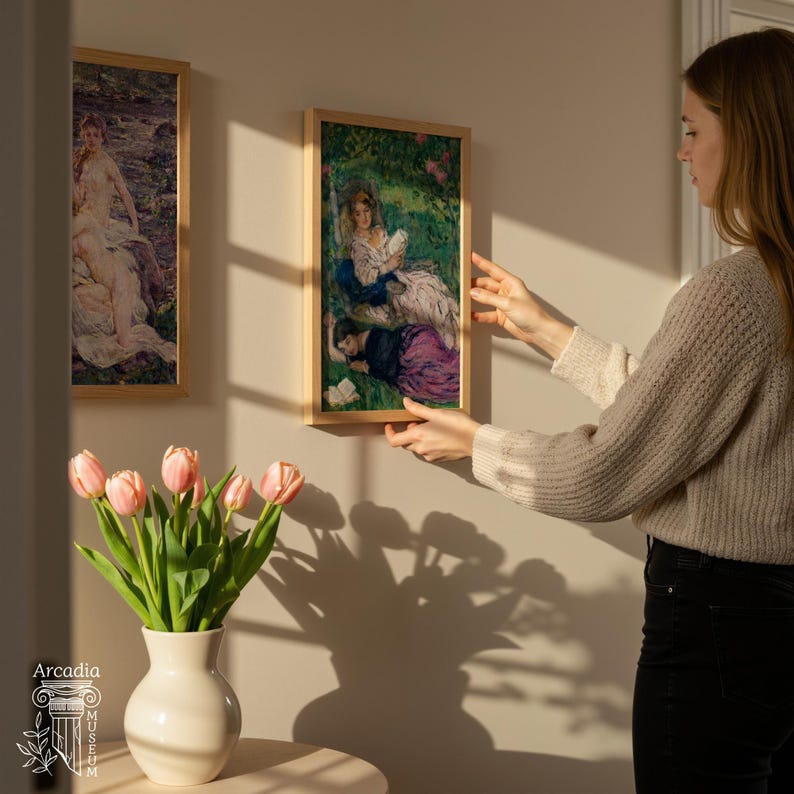 May include: Two rectangular framed art prints featuring classical paintings of figures in outdoor settings, displayed on a wall. A white ceramic vase filled with pink tulips sits on a surface in the foreground, with the Arcadia Museum logo visible.
