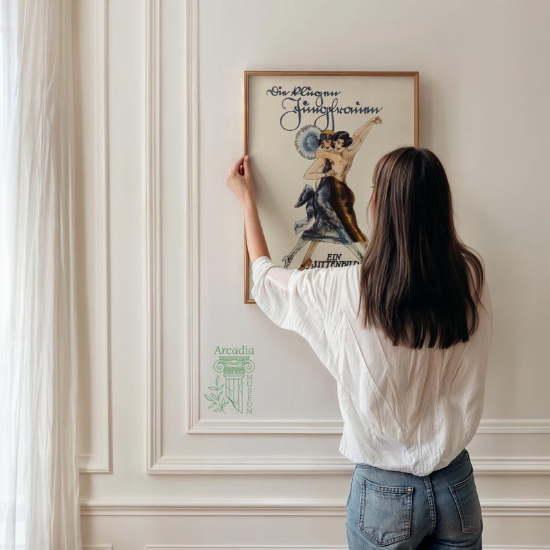 Op de afbeelding: Een ingelijste vintage poster getiteld Die Klugen Jungfrauen Ein Sittenbild met een illustratie van twee in donkere kleding dansende figuren. De poster zit in een dunne gouden lijst en bevat elegante zwarte tekst aan de boven- en onderkant.