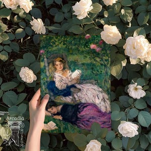 May include: A rectangular print featuring an impressionist painting of two figures in a garden, one seated reading a book and the other reclining on the grass. The artwork displays soft brushstrokes in shades of green, pink, and blue.