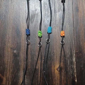 May include: Four black paracord keychains with silver swivel clips and colorful beads. The beads are blue, green, turquoise, and orange.