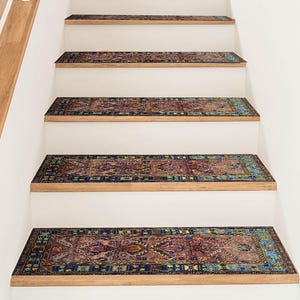 Peut inclure: Escalier avec contremarches blanches et marches en bois, orné de tapis d'escalier à motifs. Les marches présentent un motif de tapis traditionnel dans les tons de bleu, rouge et or, ajoutant une touche décorative.