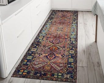 Könnte beinhalten: Ein langer, schmaler, bunter Teppich mit traditionellem persischem Design. Der Teppich hat einen dunkelblauen Rand mit komplizierten Mustern in Rot-, Orange-, Gelb- und Grüntönen. Der Teppich liegt in einer Küche mit weißen Schränken und einem Holzboden.