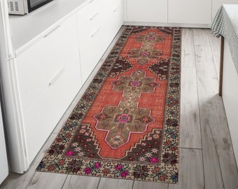 Könnte beinhalten: Ein langer, rechteckiger Teppich mit rotem und braunem Muster und floralem Design. Der Teppich liegt in einer Küche mit weißen Schränken und einer weißen Arbeitsplatte.