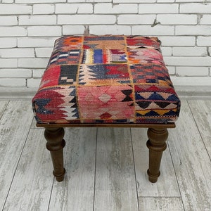 Könnte beinhalten: Ein bunter, gemusterter Ottoman mit einem Holzrahmen und gedrehten Beinen. Der Ottoman ist mit einem Patchwork-Stoff mit roten, blauen, gelben und weißen geometrischen Mustern bezogen.