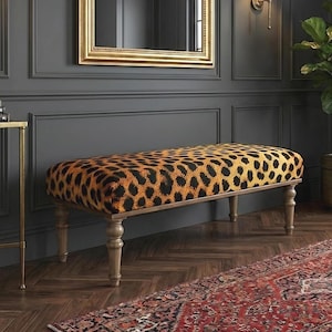 Puede incluir: Interior con paredes gris oscuro, un espejo con marco dorado y un banco con estampado de leopardo. Una pequeña mesa auxiliar dorada sostiene libros y un cuenco decorativo. Una planta en maceta y una alfombra estampada completan la decoración.