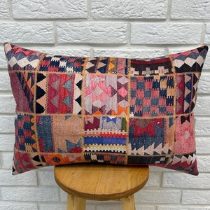 May include: A rectangular pillow with a patchwork design featuring a variety of colors, including red, pink, blue, and black. The pillow is made of a woven fabric and has a textured surface.