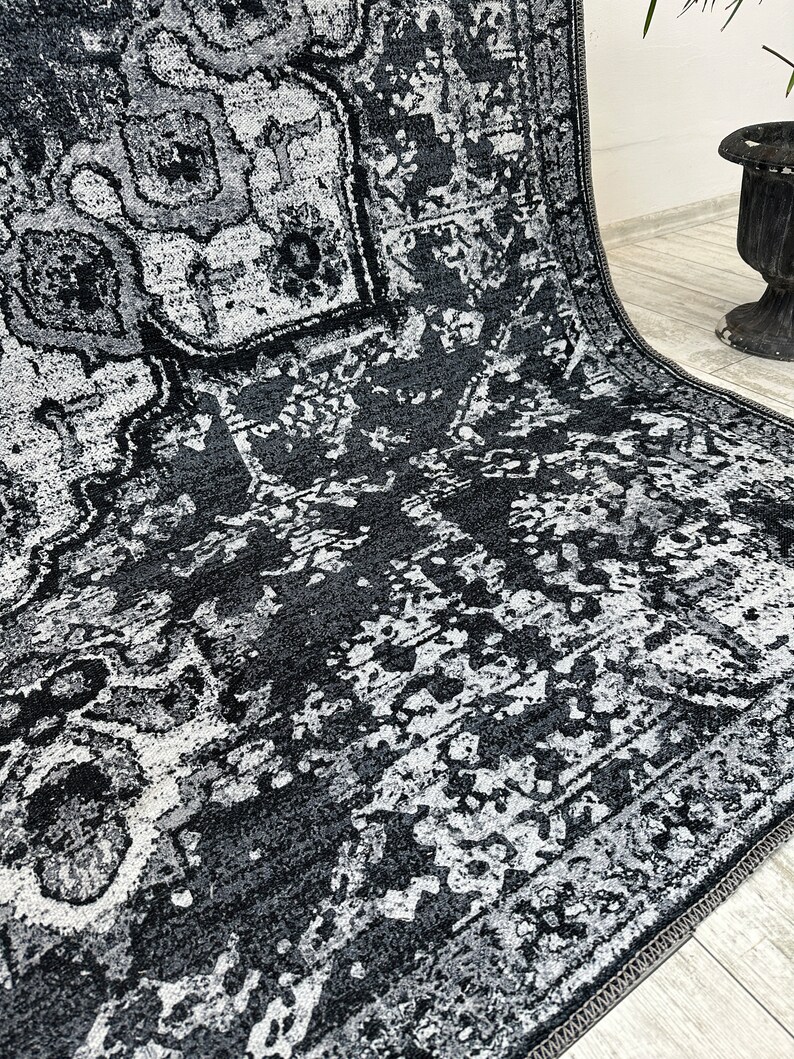 May include: A black and white area rug with a distressed, vintage look. The rug has a geometric pattern with a faded, worn appearance.