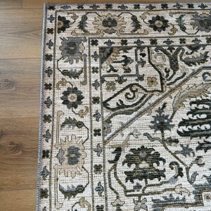 May include: A beige rug with a black and brown geometric pattern. The rug has a border with a floral design.