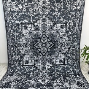 May include: A black and white area rug with a distressed, vintage look. The rug features a large, intricate medallion design in the center.