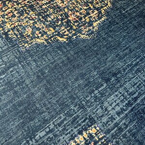 May include: A dark blue rug with a patterned design in shades of gold, orange, and red. The pattern is intricate and detailed, and the rug has a soft, plush texture.
