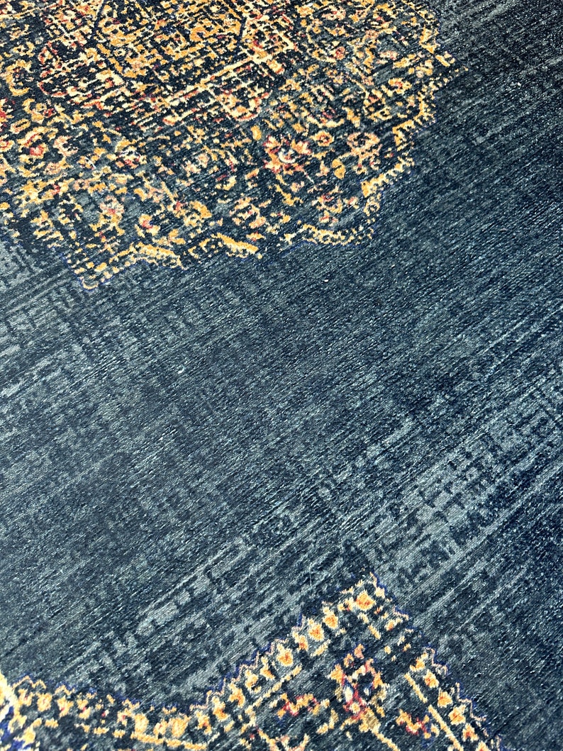 May include: A dark blue rug with a patterned design in shades of gold, orange, and red. The pattern is intricate and detailed, and the rug has a soft, plush texture.