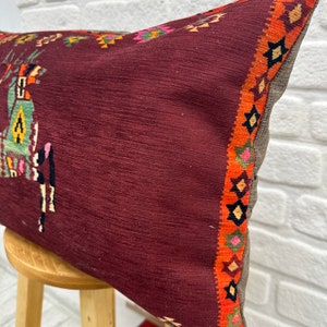 May include: A burgundy pillow with a colourful geometric pattern on the border. The pillow is made of a soft, textured fabric and has a subtle sheen.