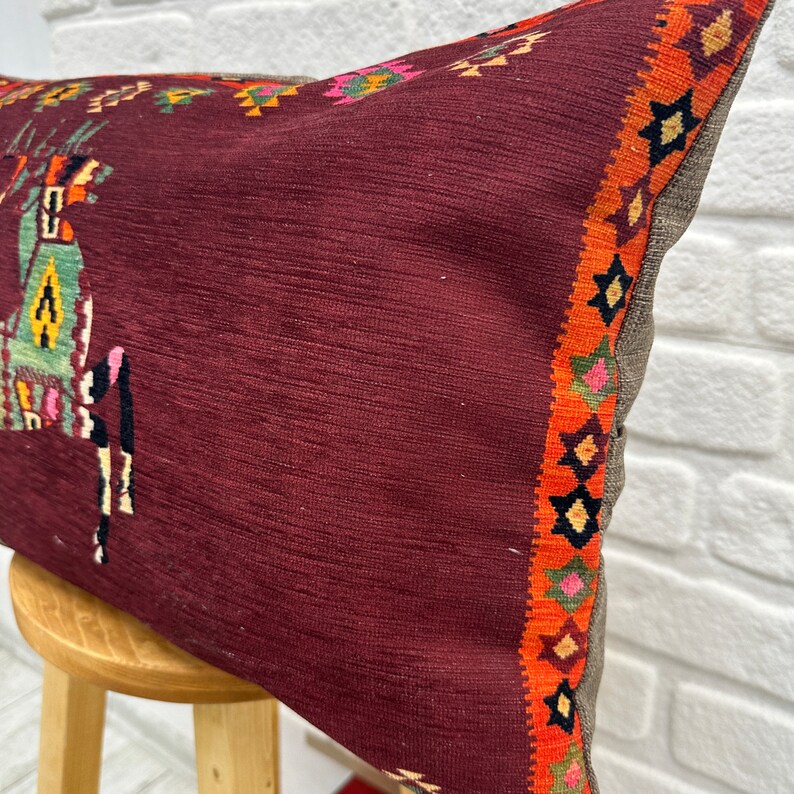 May include: A burgundy pillow with a colourful geometric pattern on the border. The pillow is made of a soft, textured fabric and has a subtle sheen.