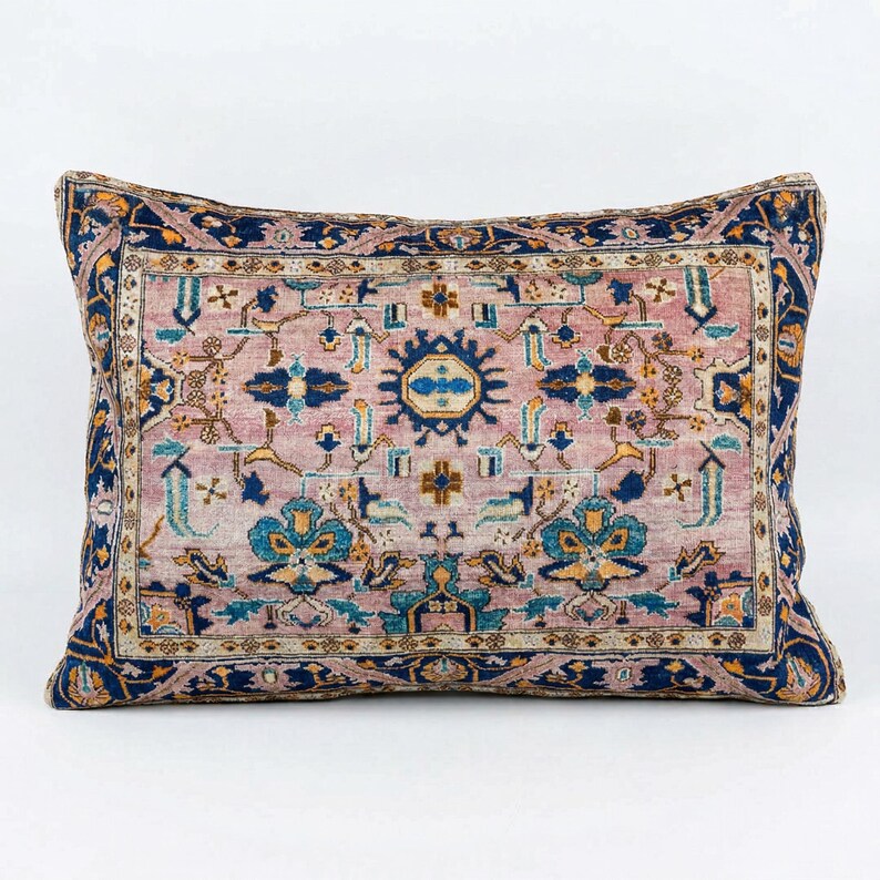 May include: Rectangular decorative pillow with a vintage rug design. The pillow features a central field of muted pink with intricate patterns in blue, teal, and gold. A dark blue border frames the design, creating a classic, elegant look.