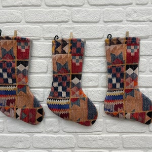 May include: Three colorful Christmas stockings with a geometric pattern, hanging on a white brick wall.