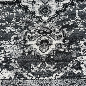 May include: Black and white area rug with a distressed, vintage look. The rug has a repeating pattern of intricate designs.