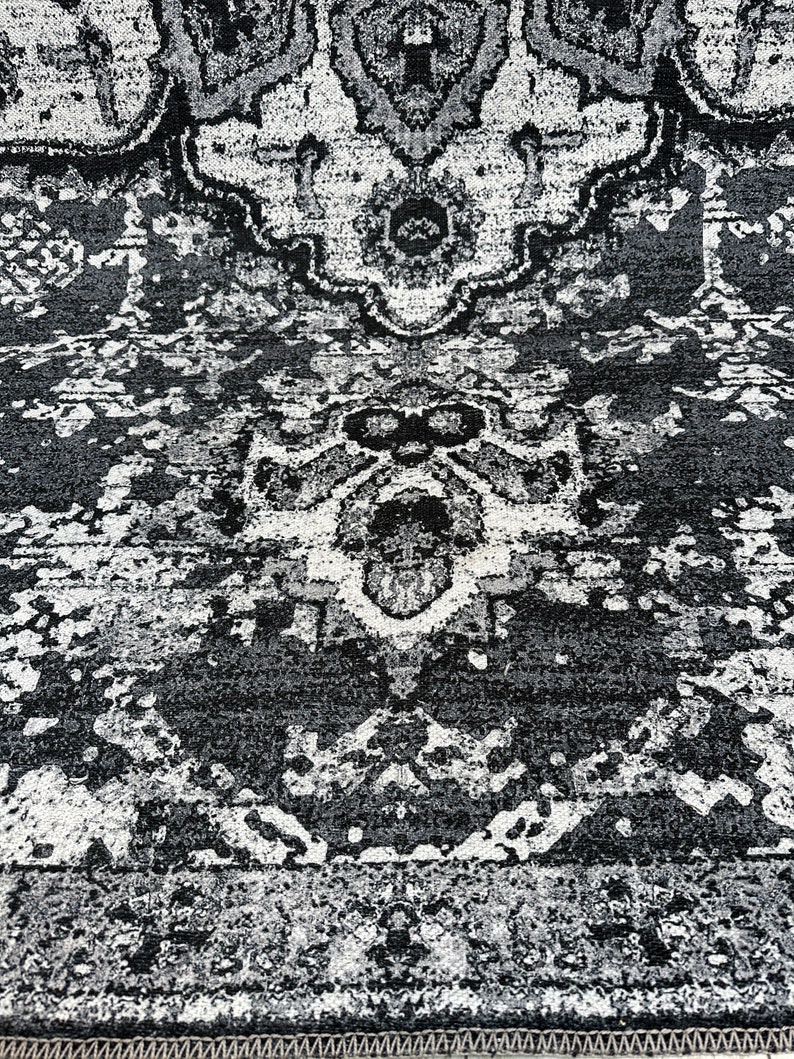 May include: Black and white area rug with a distressed, vintage look. The rug has a repeating pattern of intricate designs.