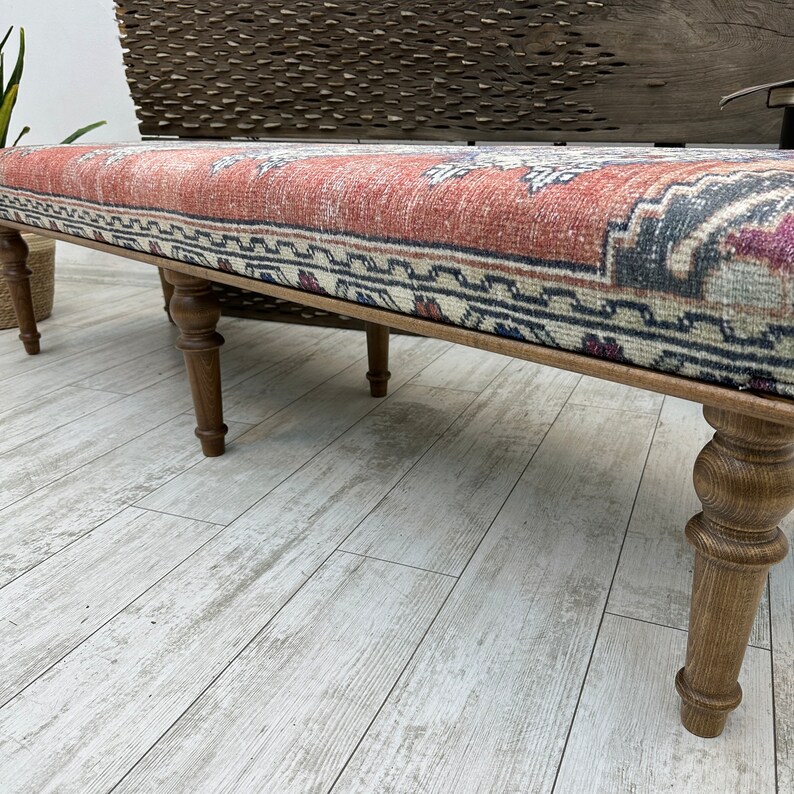 May include: A wooden bench with turned legs and a colorful patterned cushion. The cushion has a red, blue, and white geometric design.