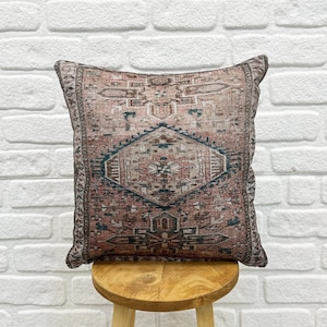 May include: A decorative throw pillow with a pink and teal geometric pattern. The pillow is sitting on a wooden stool.