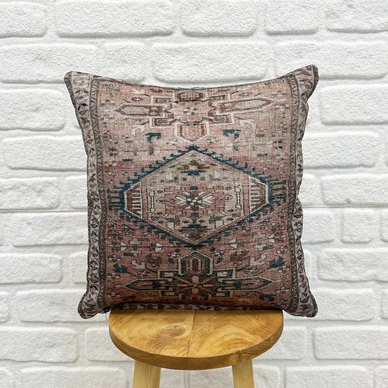 May include: A decorative throw pillow with a pink and teal geometric pattern. The pillow is sitting on a wooden stool.