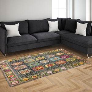 May include: A colorful patterned rug with a dark blue background and a variety of colors, including yellow, green, red, and pink. The rug is laid out on a hardwood floor in front of a gray sectional sofa.