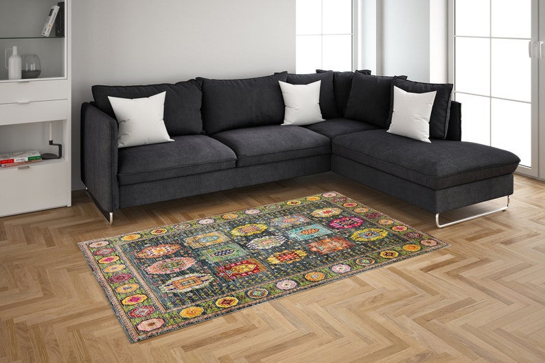 May include: A colorful patterned rug with a dark blue background and a variety of colors, including yellow, green, red, and pink. The rug is laid out on a hardwood floor in front of a gray sectional sofa.