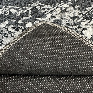 May include: Close-up of the underside of a gray and white patterned rug. The rug has a black, textured backing.