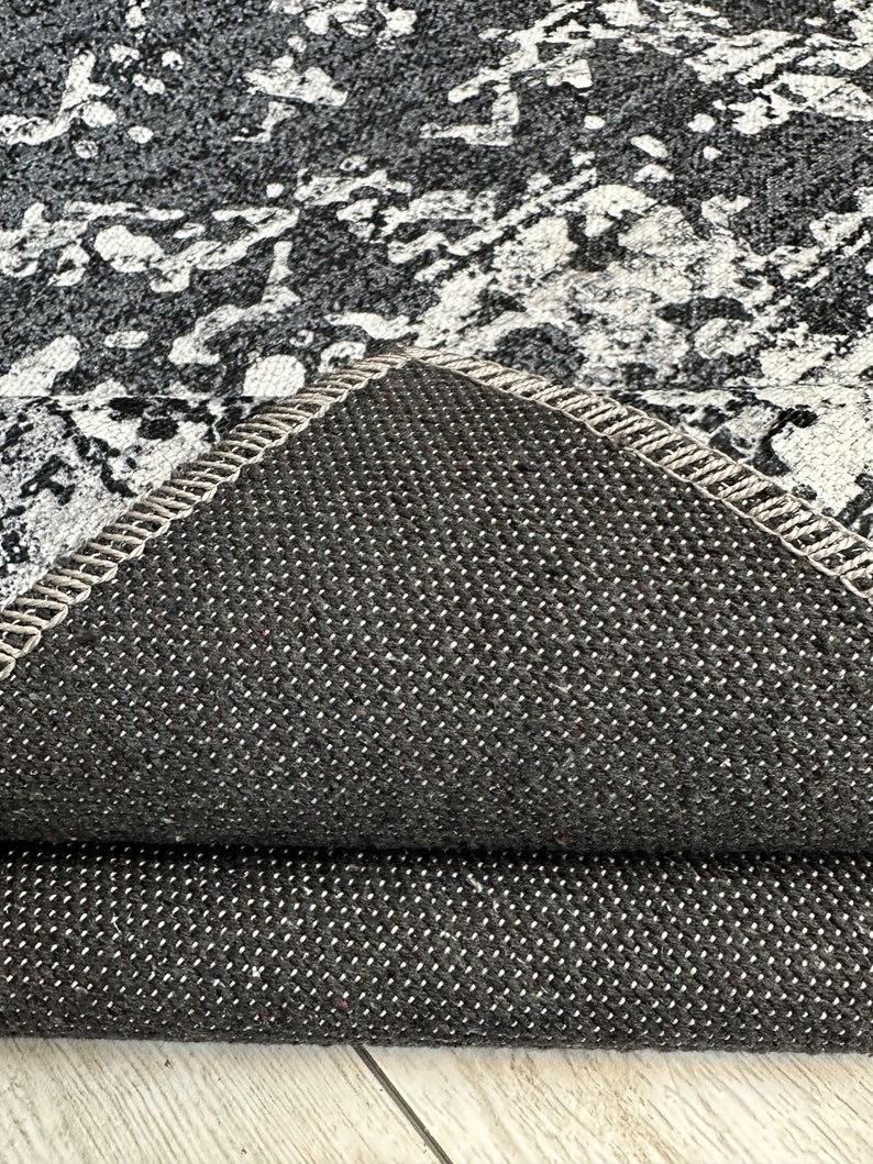 May include: Close-up of the underside of a gray and white patterned rug. The rug has a black, textured backing.