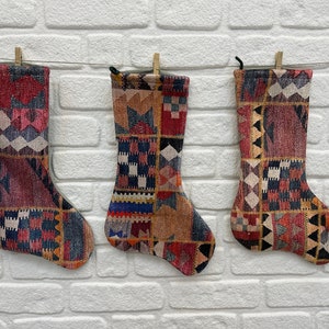 May include: Three colorful Christmas stockings with a geometric pattern hang on a white brick wall.