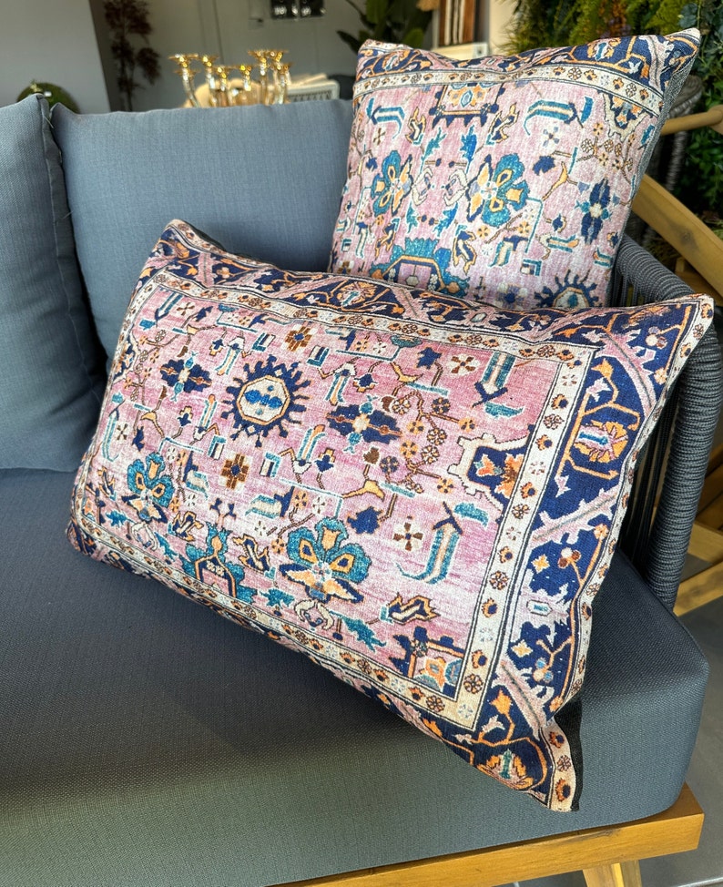 May include: Two decorative throw pillows with a vintage rug design. The pillows feature a pink and blue floral pattern with a navy blue border. They are placed on a gray outdoor sofa, creating a cozy and stylish look.