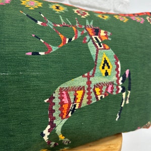 May include: Green cushion with a colourful geometric deer design. The deer is outlined in black and has a red, orange, yellow and blue pattern.