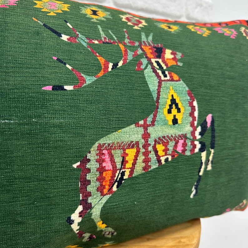 May include: Green cushion with a colourful geometric deer design. The deer is outlined in black and has a red, orange, yellow and blue pattern.